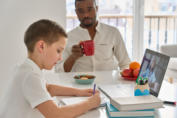 Caucasian teenage school boy son distance learning remote online zoom class with web teacher doing homework sitting at home table with African Black father. Virtual education concept.