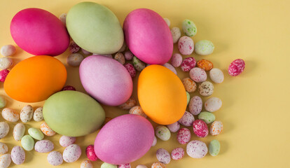 Fototapeta na wymiar Colorful Easter eggs with colored candies on a yellow background top view flat lay