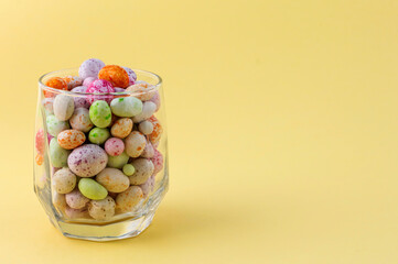 glass cup with colored candies on a yellow background with a copy of the space