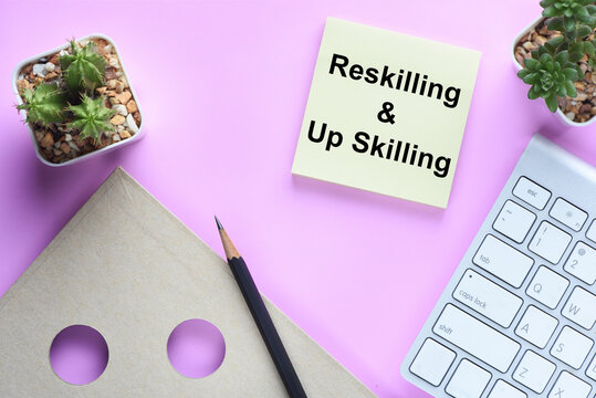 Reskilling and up skilling written on sticky note on workspace. New skills development concept and changing skill demand idea.