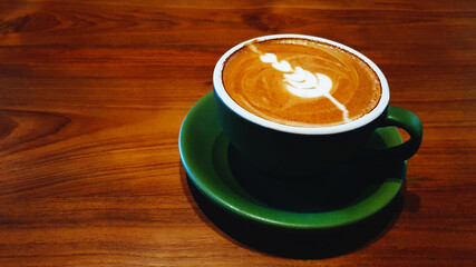 Cup of art cappuccino or latte coffee on brown wooden background.  Hot drinking in green glass at café shop with copy space. Food design concept.