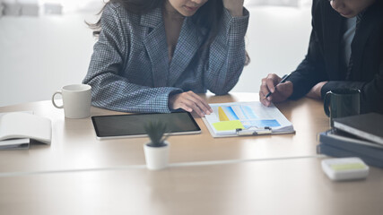 Cropped shot of two business colleagues using digital tablet an analyzing business data on paper at office.