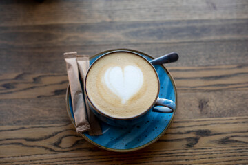blue cup with coffee with heart-shaped froth on the table with a bag of sugar.cup,