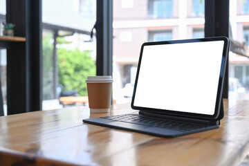 Close up view of mock up compute tablet and coffee cup on wooden table near window.