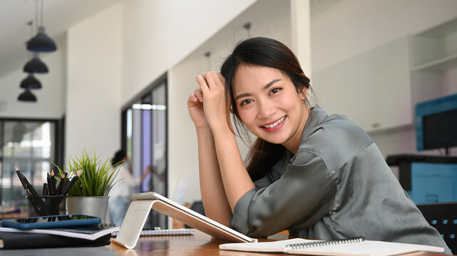 Happy young woman sitting at her workplace and smiling to camera.