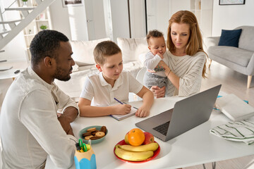 Multiracial parents helping teenage son distance studying at home. Caucasian teen school boy learning virtual zoom class remote homeschooling on laptop computer doing homework with diverse family.