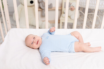 Obraz na płótnie Canvas happy baby lies in the crib, cute little boy of six months lies in the nursery on the bed