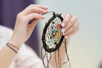 Women's hands hold a dream catcher-an accessory made of tree branches, macrame threads and beads.