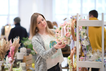 business owner selling behind counter with her bouquet of dried flowers at local market of craftsmen, small business. young woman entrepreneur sells floral holiday composition.