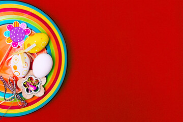 Easter composition with eggs, flowers and a rainbow on a red background. Orange plate. Red background. Place for text. Happy Easter.