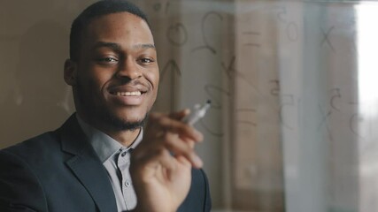 Alone afro-american business man male leader standing on modern office, writing ideas formula, counting finance profit on glass transparent board, working analyzes strategy, smiling with good results - Powered by Adobe
