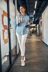 Elegant lady with a laptop and a mug walking ahead
