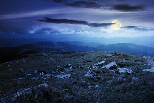 carpathian summer mountain landscape at night. beautiful countryside with rocks on the grassy hill in full moon light clouds on the blue sky. wonderful travel destination