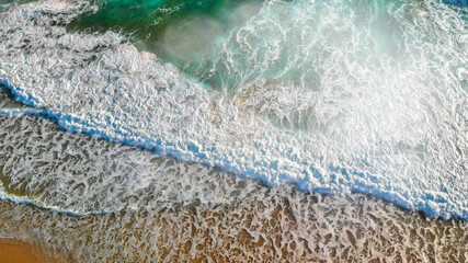 Waves along the shoreline at sunset, aerial view from drone