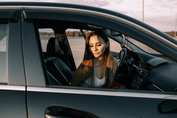 Beautiful young girl driving a car in the evening in the sunset sun on an empty parking lot