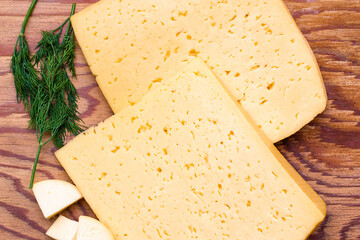 two large pieces of cheese on a wooden table surrounded by greenery and small pieces of cheese