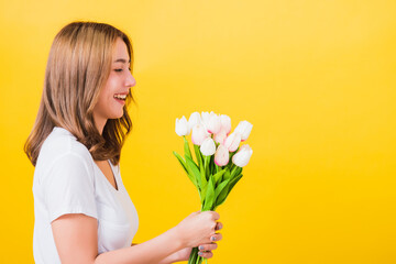 Portrait Asian Thai beautiful happy young woman smiling, screaming excited hold flowers tulips bouquet in hands and she looking to flowers, studio shot isolated on yellow background, with copy space