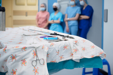 Selective focus on a surgical clamp close-up on a table with other instruments during a surgical operation. Unidentified medical workers on a blurred background.