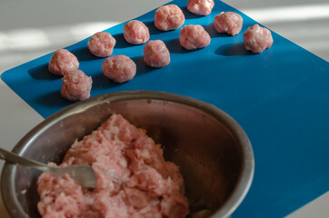 Raw meatballs and metal bowl with minced meat and fork on blue.