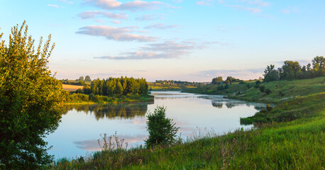 Fototapeta na wymiar Summer serene landscape with calm river and green hills at sunrise.