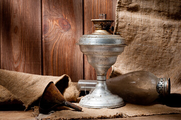 A vintage kerosene lamp covered in dust and soot, shot against a background of wood panels and burlap.