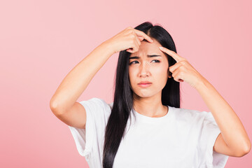 Fototapeta premium Portrait teenage Asian beautiful young woman having skin problems squeezing pimples on her face, studio shot on pink background, with copy space, Thai female acne, beauty care concept