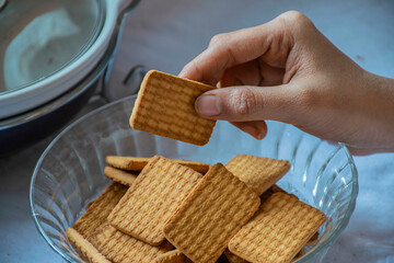 Stock photo of a women taking wheat biscuit from a bowl of biscuits , kept on table on white background. focus on biscuit.