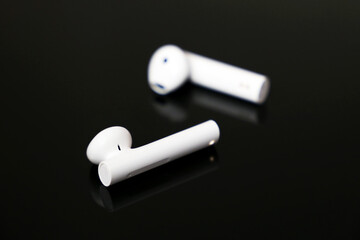 White wireless earphones on black glass table. Headset for listening to music and voice call
