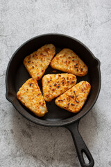 Hash browns cooked in a cast iron frying pan.  Concrete background