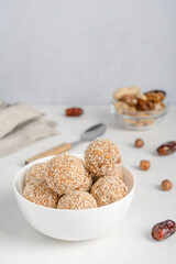 Organic sweet truffles dessert or homemade nut vegan energy balls made of sesame, hazelnut and dates fruit served in bowl on white wooden table with textile against gray wall. Vertical image