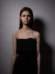Naklejka premium Beautiful woman with red hair in a black dress on a gray background bared shoulders