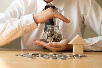 Man's hand protects glass bottles, saves money with coins, steps towards real estate Investment savings concept