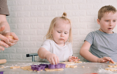 kids help their mom to make delicious cookies at home in the kitchen. joint cooking is a concept of...