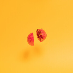 two half of fresh red tropical pomegranate flies in the air on the yellow sunny summer background. abstract art. minimal creative idea.