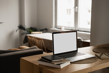 Obraz na płótnie Canvas Laptop with blank copy space screen on table with notebooks on wooden table. Minimalist home office workspace. Mockup template.