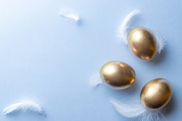 Easter Golden colour eggs in basket with spring tulips, white feathers on pastel blue background in Happy Easter decoration. Festive decoration in flat lay.
