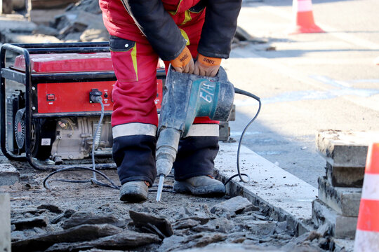 Worker repair the road surface with a jackhammer. Construction work, laying of paving slabs in city