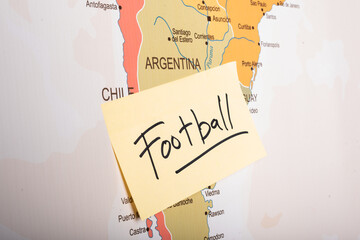 football written on a sticky note attached with the Argentina country on world map.