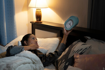 Focus alarm clock . Beauty hispanic woman  in robe at home bedroom lying on bed late at night trying to sleep suffering insomnia.
