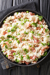Risi e Bisi classic Italian comfort food of rice with peas and chunks of ham close up in a plate on the table. Vertical top view above