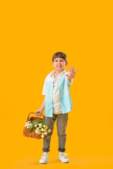 Cute little boy with bouquet of flowers in basket on color background