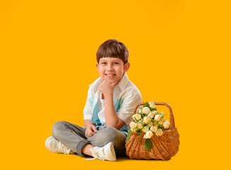 Cute little boy with bouquet of flowers in basket on color background