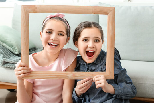 Portrait of cute twin girls with photo frame at home