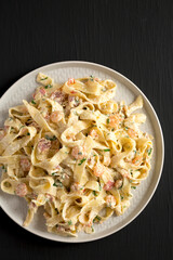 Homemade Garlic Shrimp Bacon Alfredo on a plate on a black surface, top view. Flat lay, overhead, from above. Copy space.