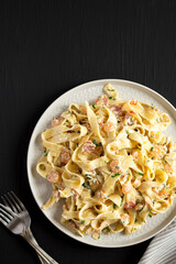 Homemade Garlic Shrimp Bacon Alfredo on a plate on a black background, top view. Flat lay, overhead, from above.