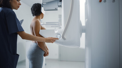Friendly Female Doctor Adjusts Mammogram Mashine. Topless Latin Female Patient with Curly Hair...