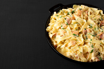 Homemade Garlic Shrimp Bacon Alfredo in a cast-iron pan on a black background, low angle view. Copy space.