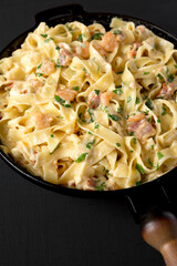 Homemade Garlic Shrimp Bacon Alfredo in a cast-iron pan on a black surface, side view.