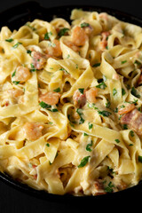 Homemade Garlic Shrimp Bacon Alfredo in a cast-iron pan on a black background, side view. Close-up.