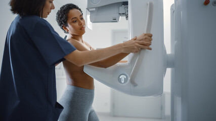 Fototapeta na wymiar Friendly Female Doctor Explains the Mammogram Procedure to a Topless Latin Female Patient with Curly Hair Undergoing Mammography Scan. Healthy Female Does Cancer Prevention Routine in Hospital Room.